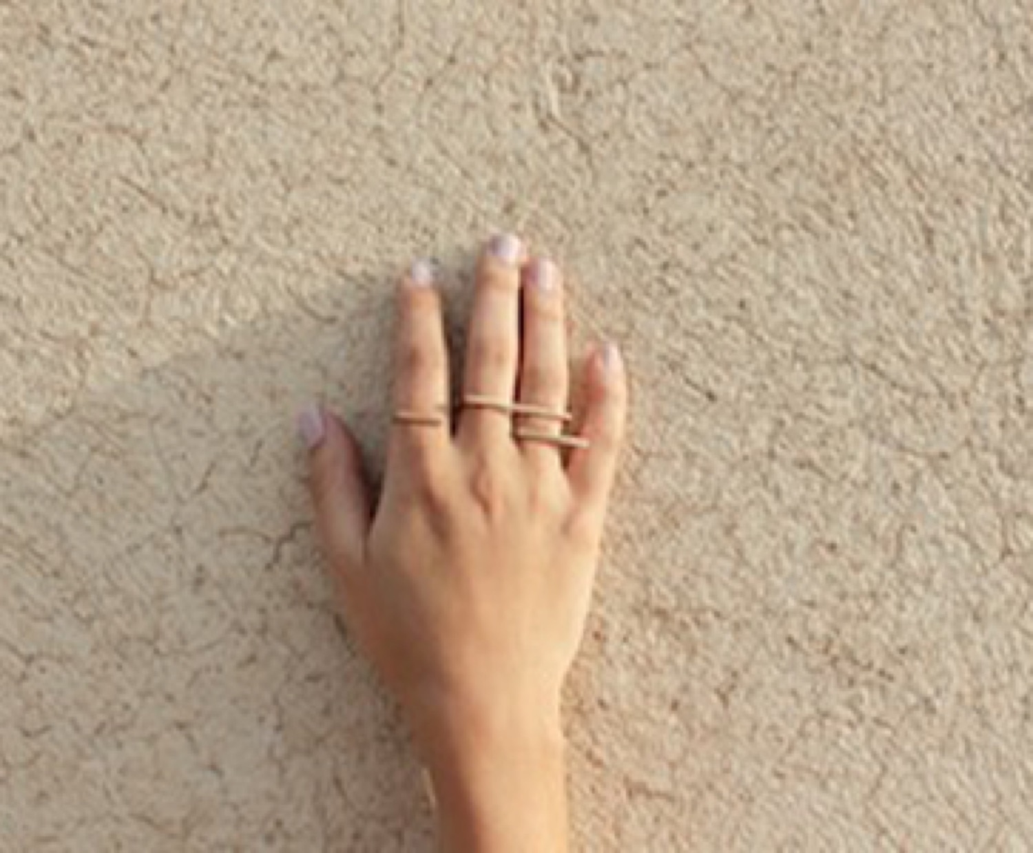 A hand on a textured earth wall, rings catching the light
