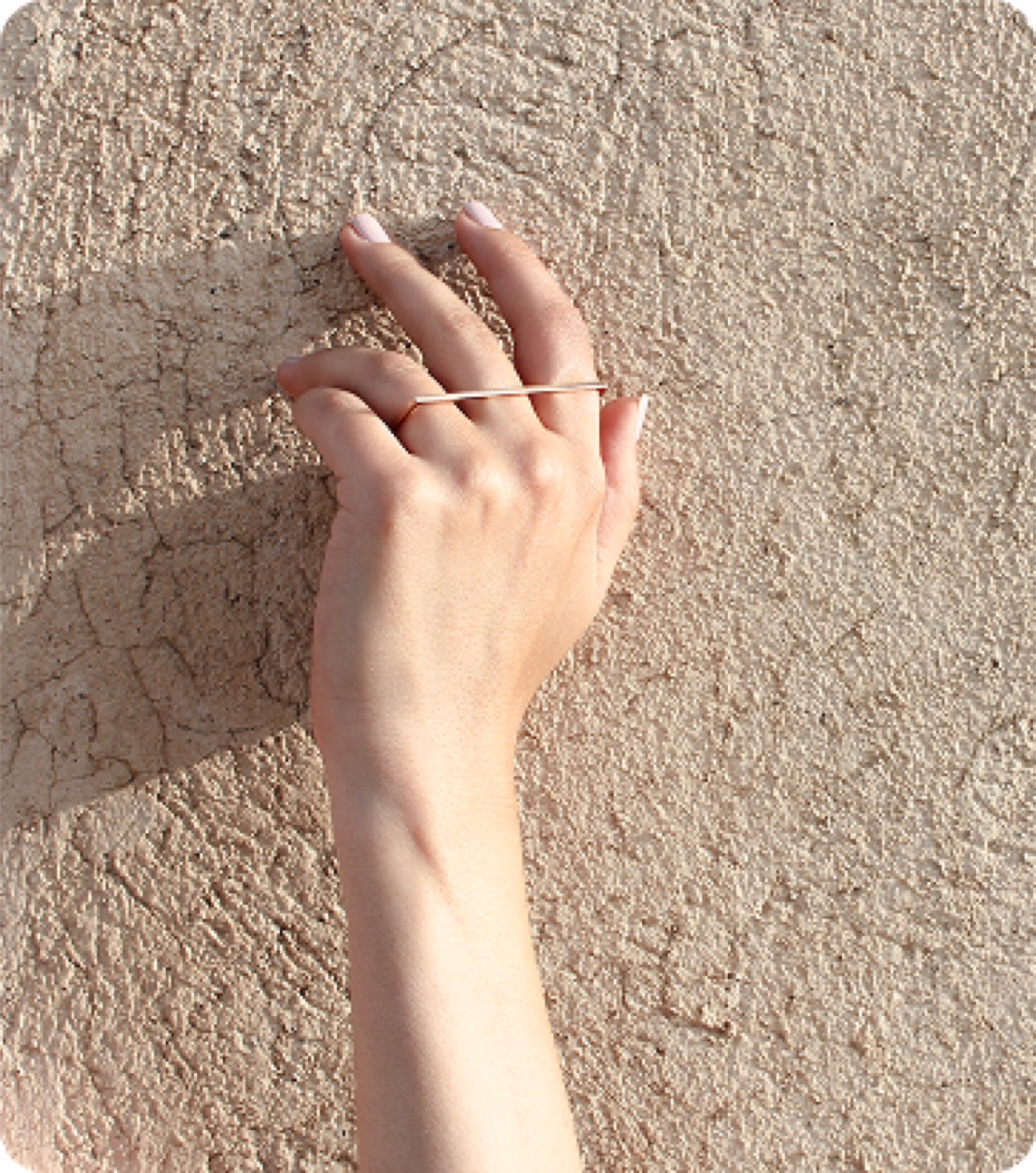 A hand pressed flat on an earth wall, wearing stacked rings
