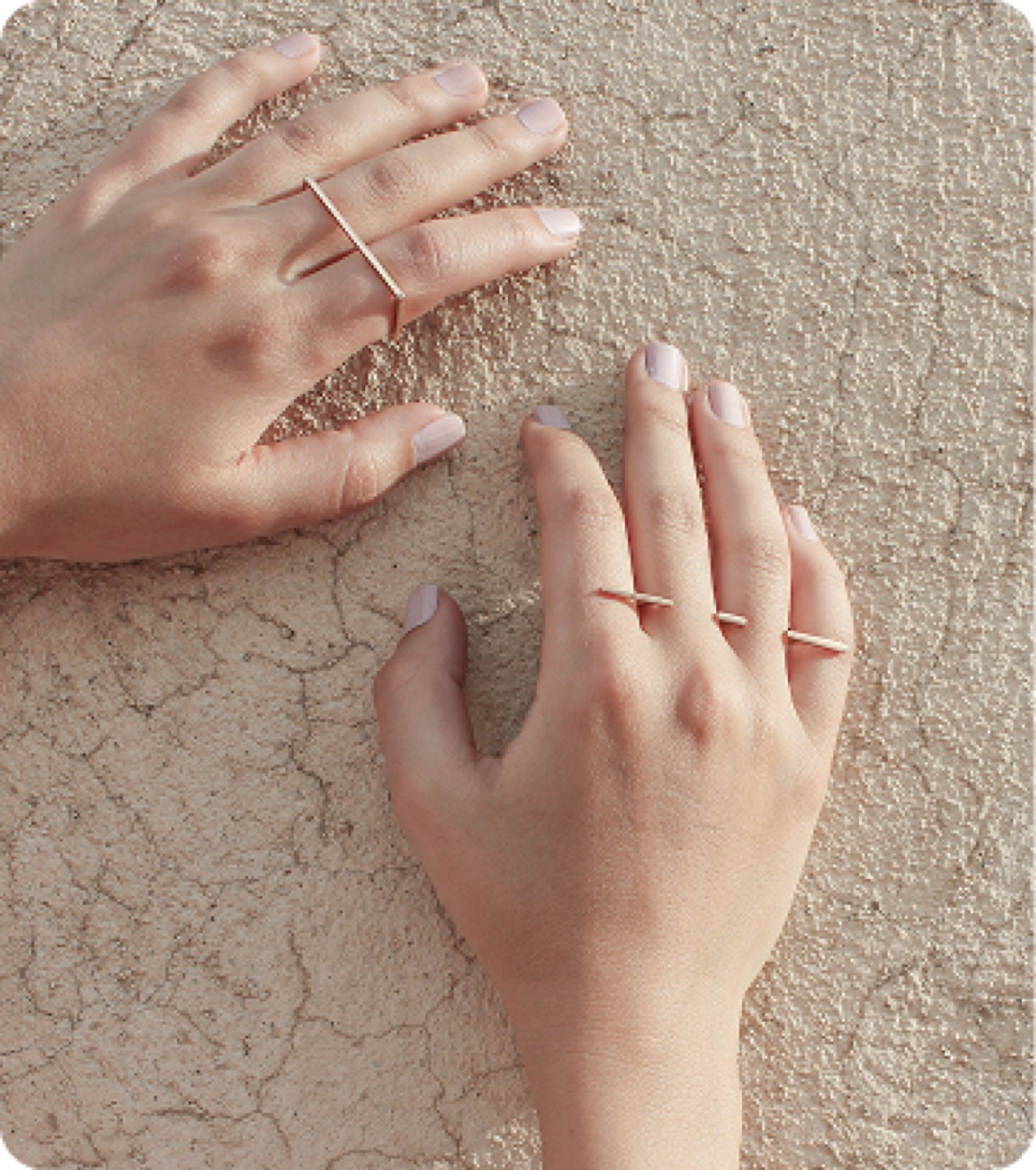 Two hands resting on cracked earth, both wearing line rings