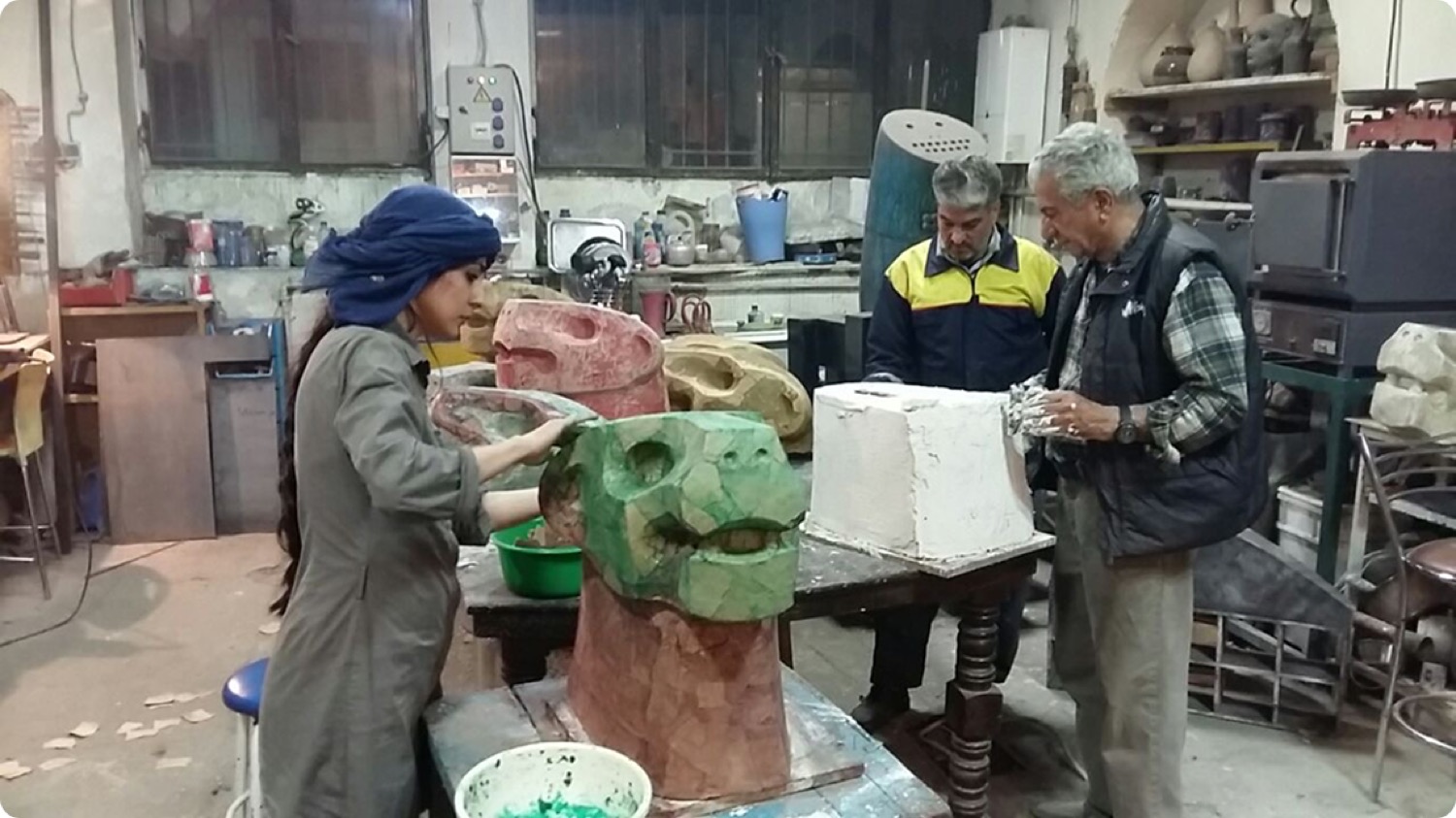 Ladan Johari working on a large ceramic form in a casting workshop alongside two colleagues